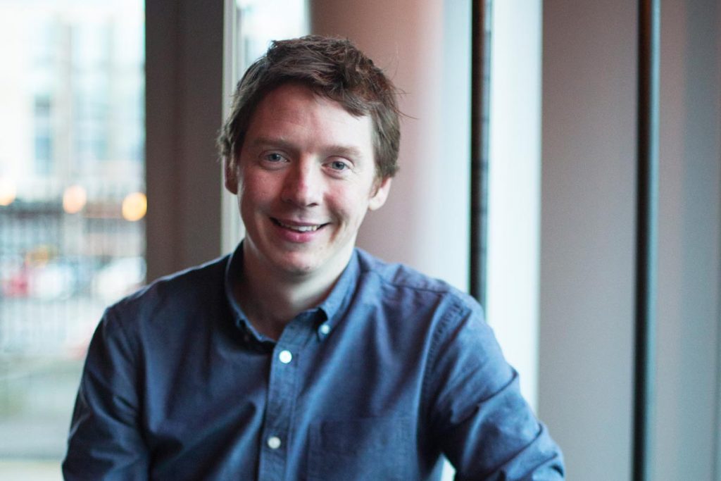 A headshot of Kevin McGrath sitting in a coffee shop wearing a blue shirt.